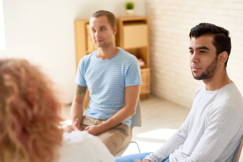 Two young men listen another speaks to the group. This could represent group therapy in Pasadena, CA. Learn more about group trauma therapy in Pasadena, CA, our LGBTQ support group in Sacramento, CA, and other services.