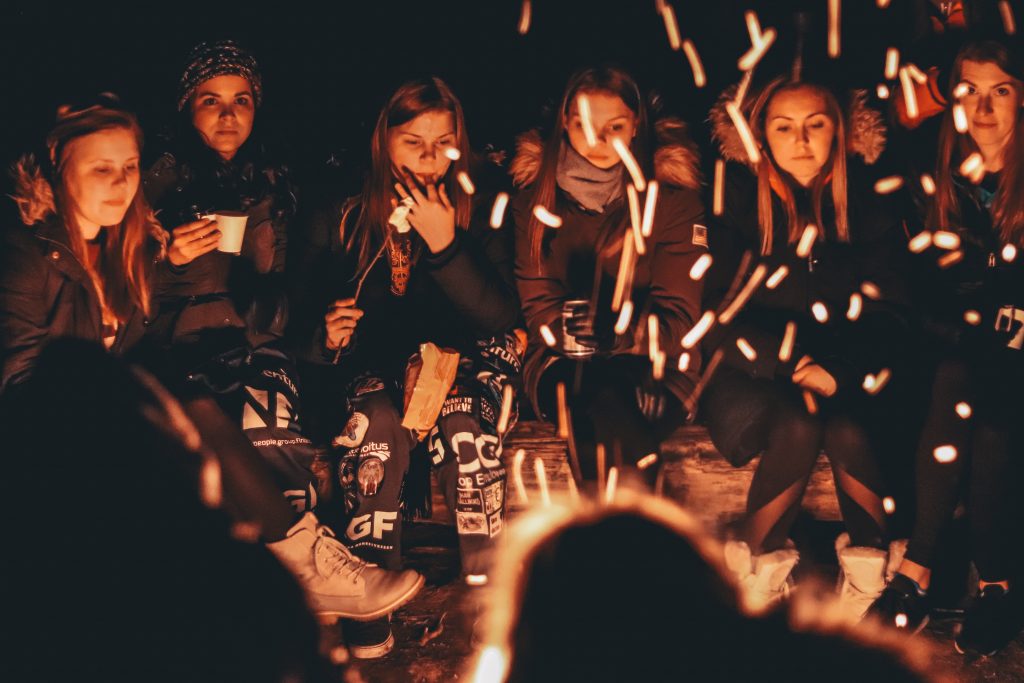 A group of woman sit around a campfire as they roast marshmallows. This represents group therapy in Pasadena, CA. Contact us today to learn more about our sexual abuse support group, group trauma therapy, and other services!