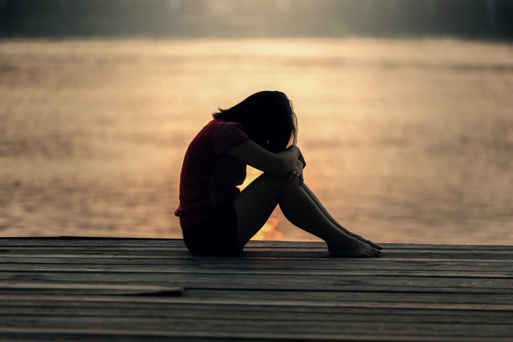 A woman sits by the side of a lake stricken with grief. Grief and loss are painful experiences. Grief counseling in Sacramento, CA 95688