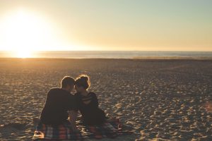 A couple sits together on the beach at sunset representing a couple who has overcome betrayal in their relationship with Marriage Counseling in Pasadena, CA.